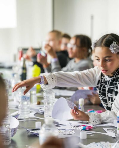 Une petite fille avec une pince en forme de fleurs dans les cheveux qui fabrique un bricolage