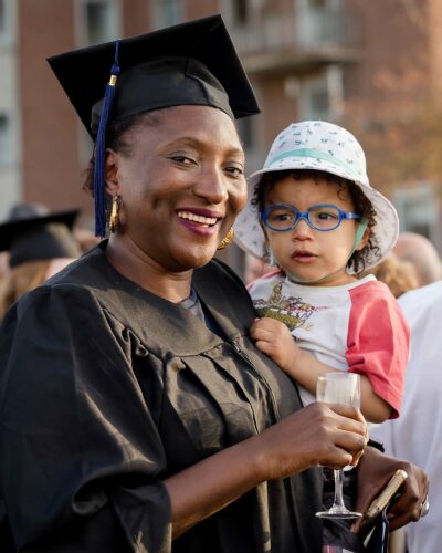 Photo académique d'une diplômée souriante en toge noire tenant un enfant dans ses bras
