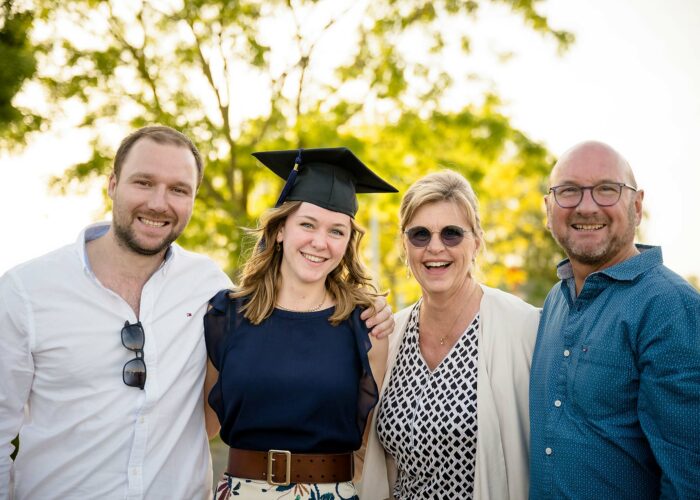 Photo académique d'une jeune diplômée en robe bleue, entourée de trois proches souriants.