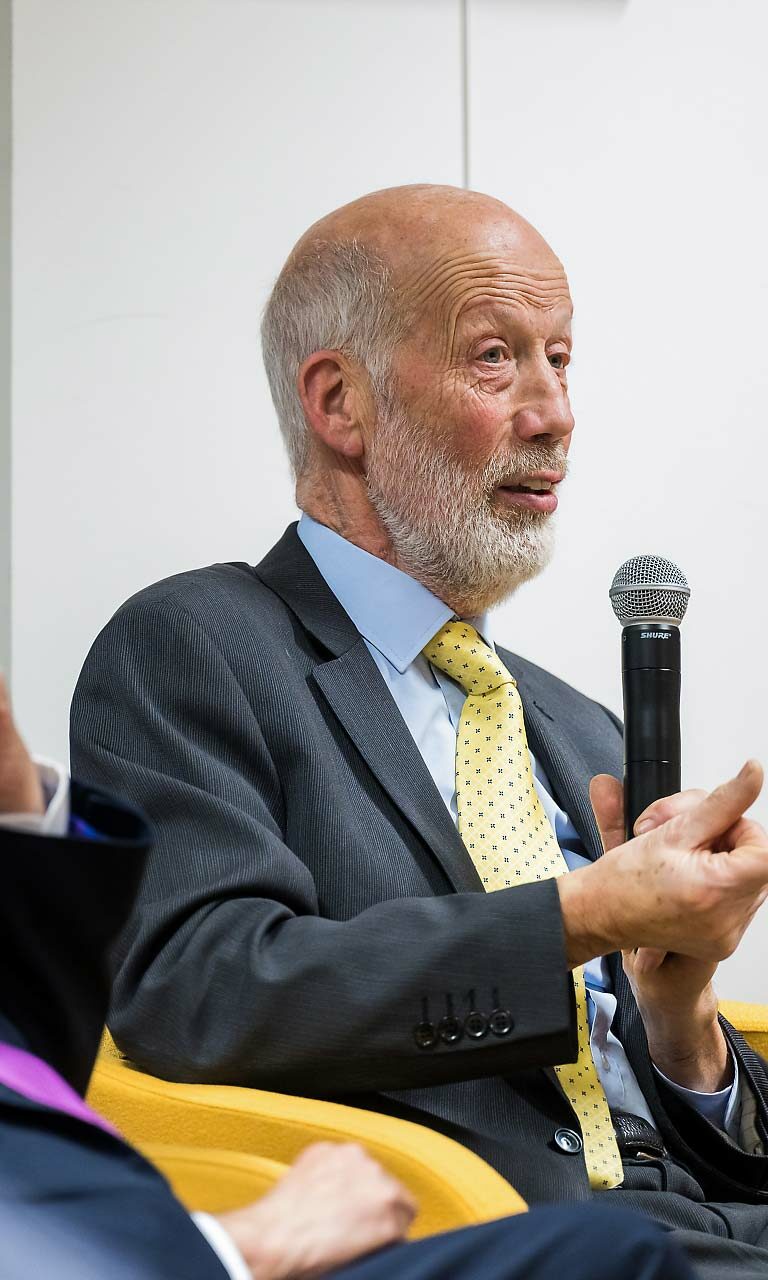 Un homme en costume et cravatte jaune qui tient un micro à main