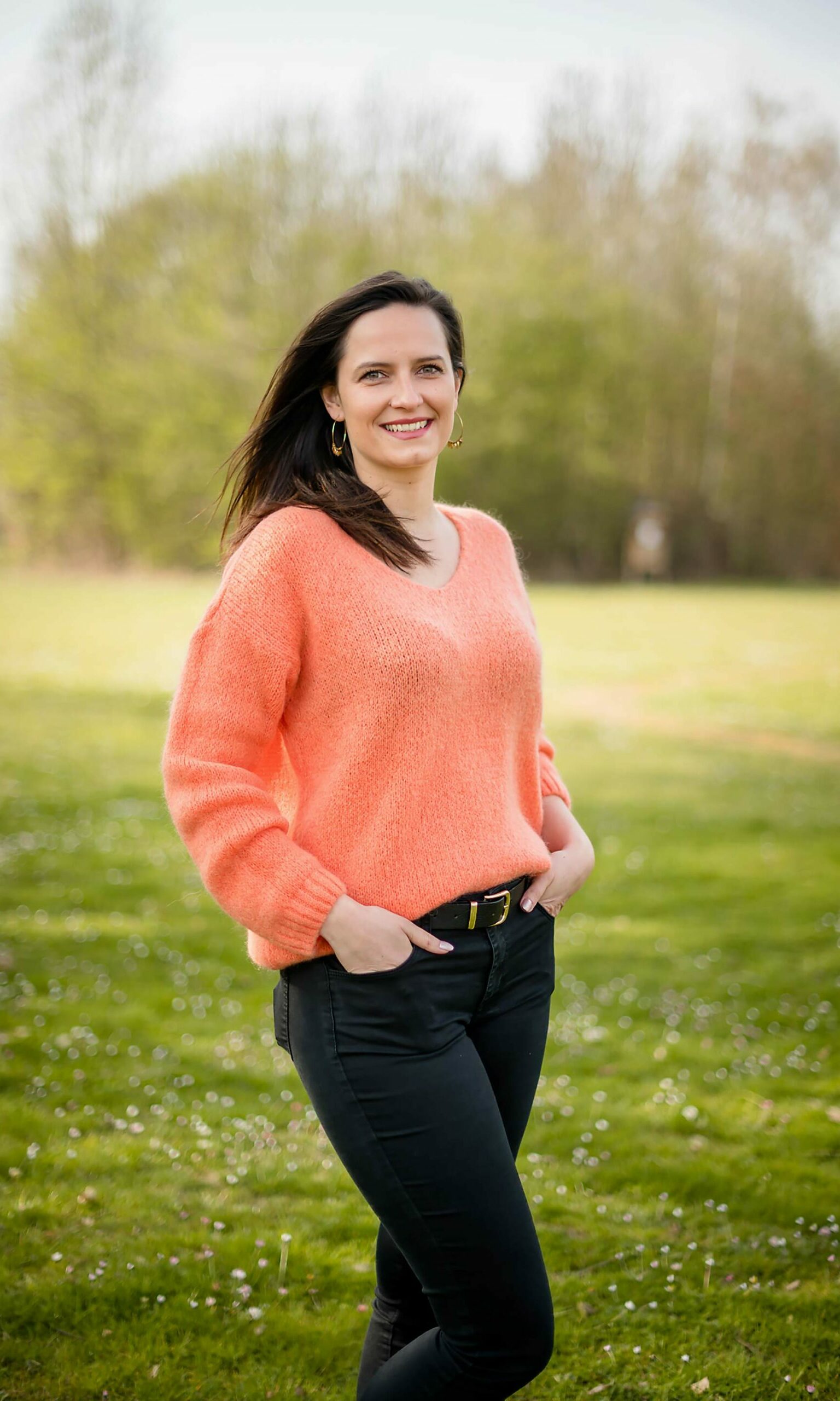 Portrait d'entreprise - une femme avec des longs cheveux bruns foncé et un pull orange dans un grand jardin