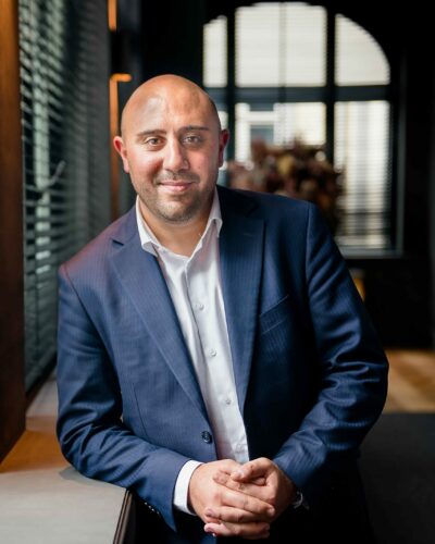 Portrait d'entreprise - un homme en costume bleu foncé qui croise les mains à côté d'une fenêtre