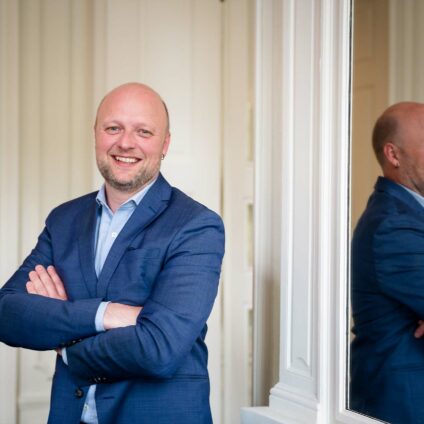 Portrait d'entreprise - un homme en costume bleu foncé et une boucle d'oreille qui se tient à côté d'un grand miroir