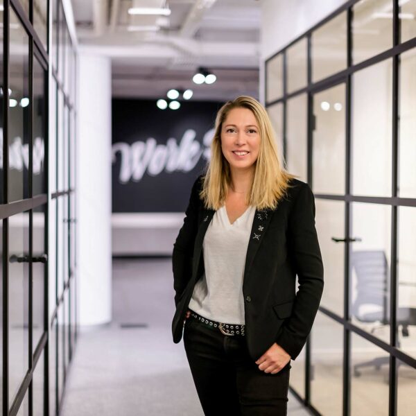 Portrait d'entreprise - Une femme aux cheveux blonds qui porte une tenue noire et blanche dans le couloir d'un coworking