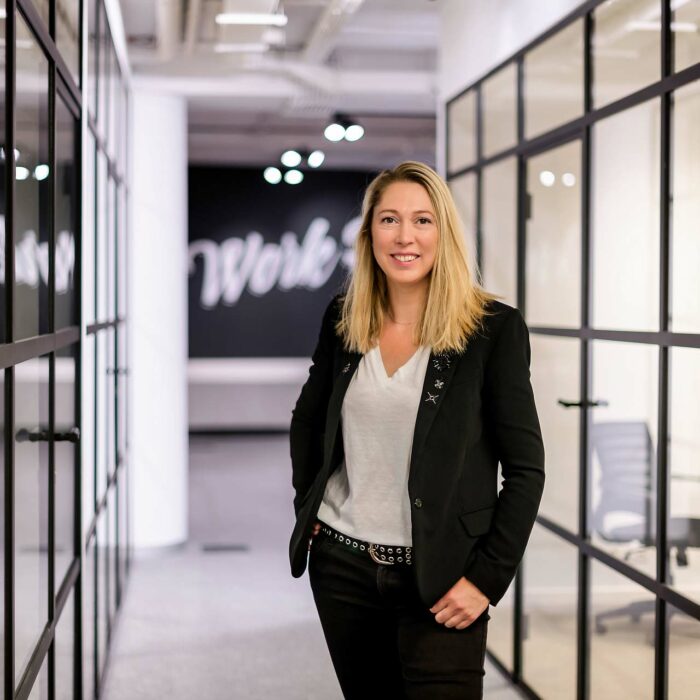Portrait d'entreprise - Une femme aux cheveux blonds qui porte une tenue noire et blanche dans le couloir d'un coworking