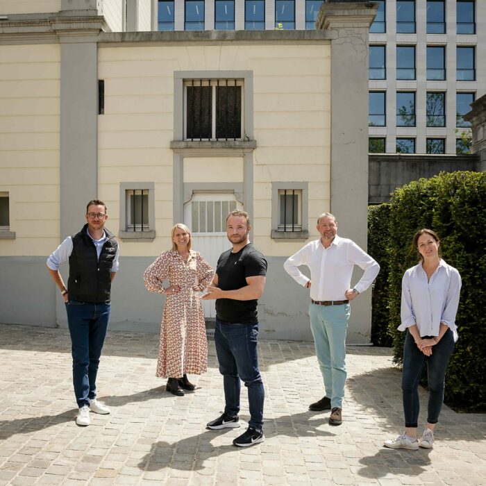 Un groupe de 5 personnes se tient dans un cour pavée devant un bâtiment historique à la façade blanche.