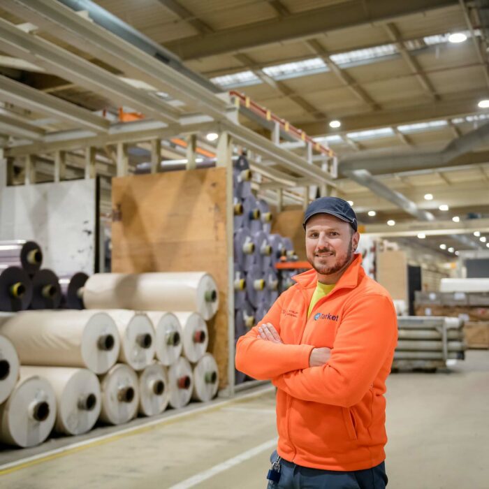 Portrait d'un ouvrier souriant vêtu d'un gilet orange dans un centre de stockage de matériel