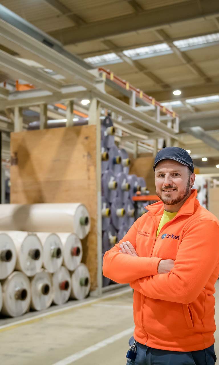 Portrait d'un ouvrier souriant vêtu d'un gilet orange dans un centre de stockage de matériel
