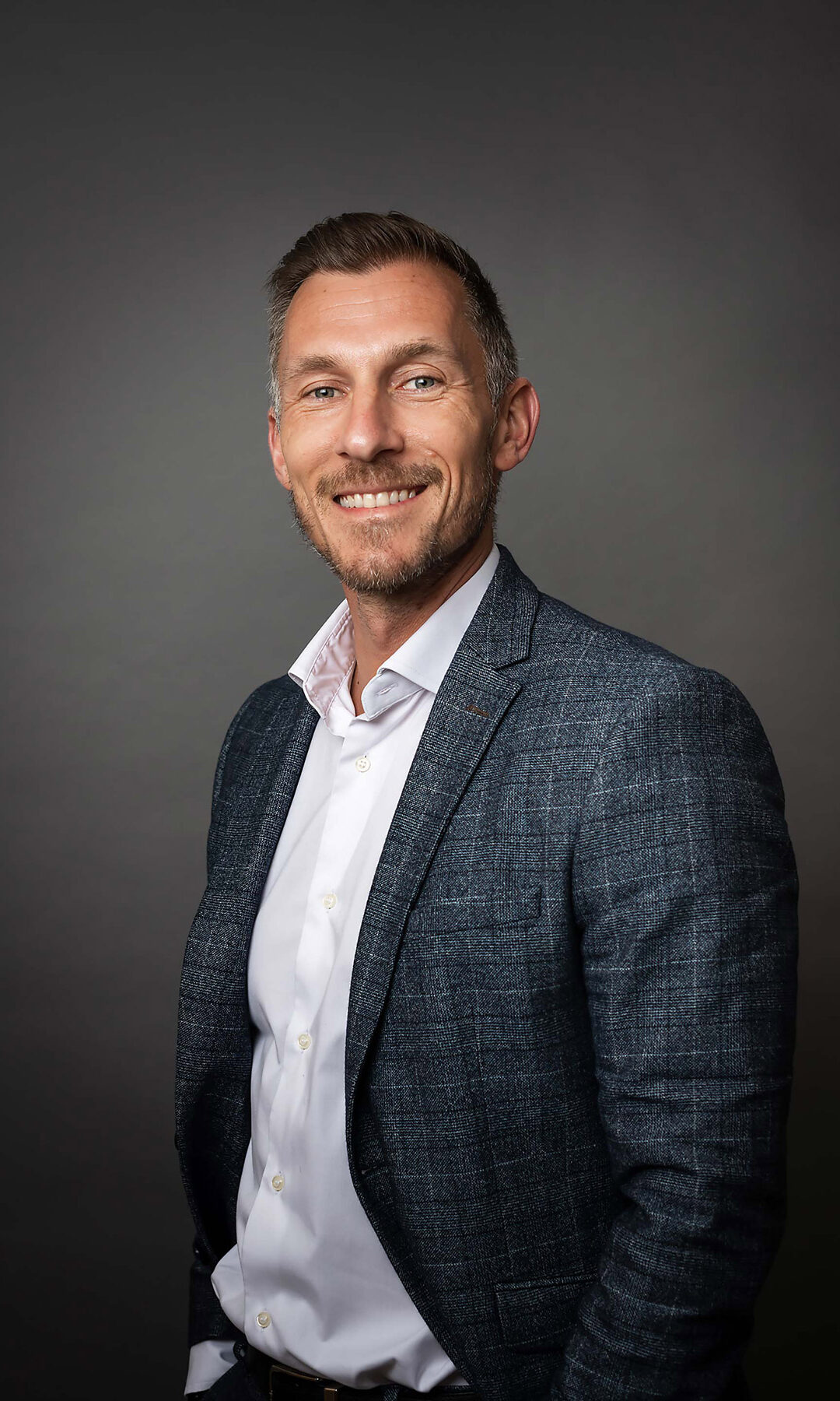Photo d'un entrepreneur souriant qui porte un costume à carreaux et une chemise blanche et qui pose devant un fond noir