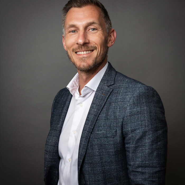 Photo d'un entrepreneur souriant qui porte un costume à carreaux et une chemise blanche et qui pose devant un fond noir