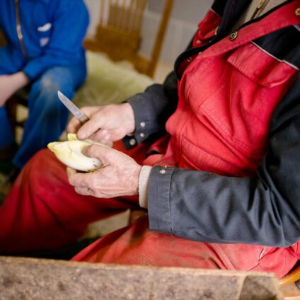 Un homme en salopette rouge et noire tient un chicon et un couteau à la main